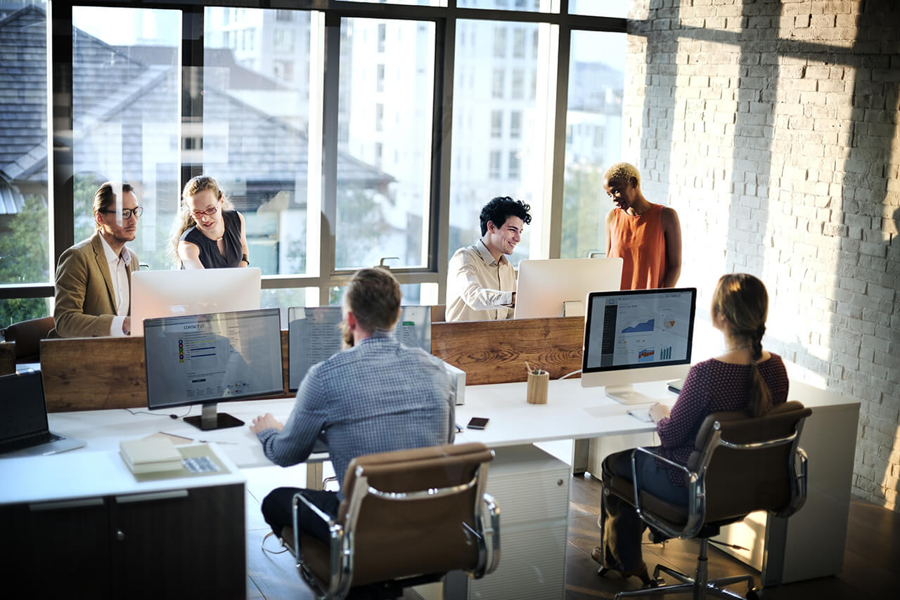 Blick in eine Art Callcenter wo IT-Dienstleister und IT-Berater am Schreibtisch vermutlich Beratungen durchführen - Arbeit und Vermögen schützen mit einer Berufshaftpflichtversicherung in der IT-Branche